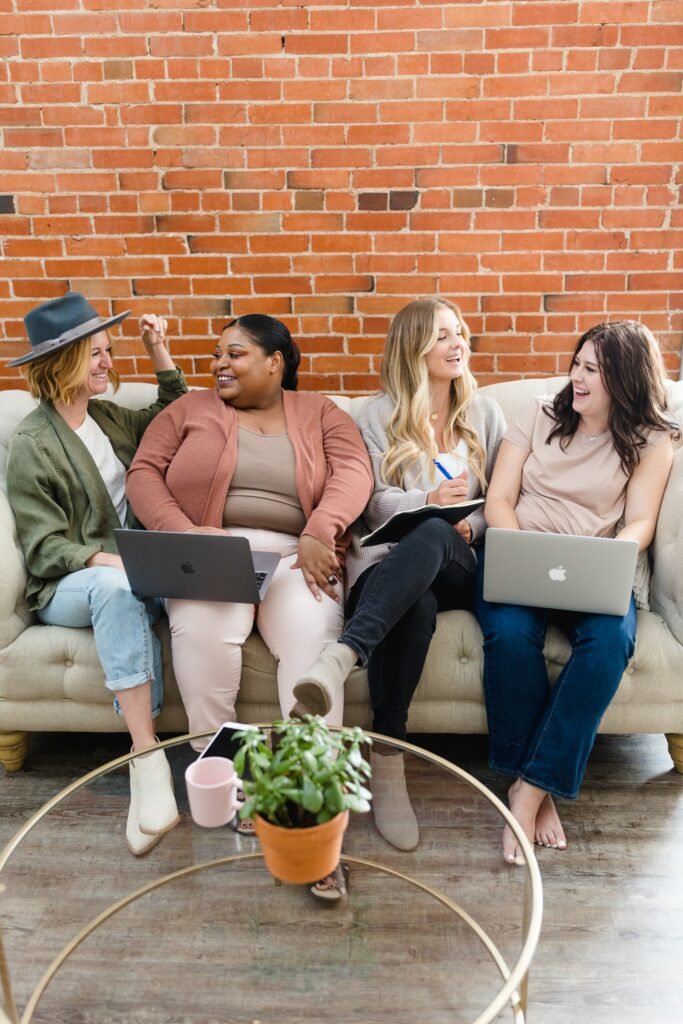 Four women seating on a couch with two laptop